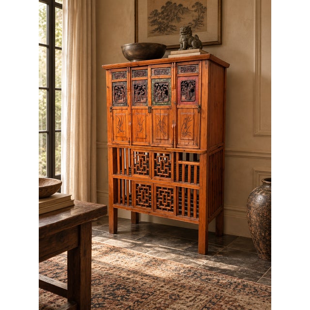 A striking vintage Chinese carved wood storage cabinet featuring detailed figural panels, incised floral decoration,...
