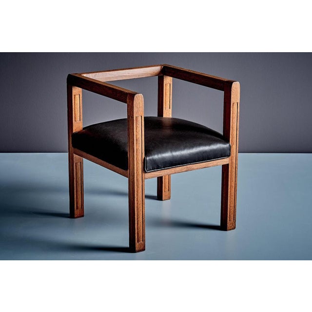 Elegant Art Deco armchair made of solid oak with carved details and a black leather seat cushion. The chair features...