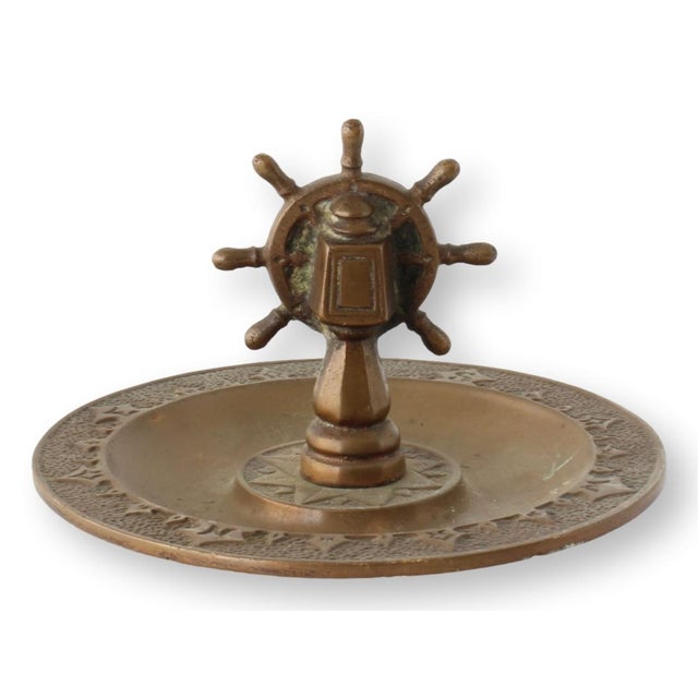 This bronze nautical ashtray features a ship's wheel mounted at its center, with a compass star and raised detailing....