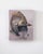 This artwork features an intricately detailed helmet, adorned with ornate embellishments, set against a soft, muted...