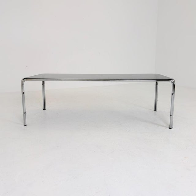 A striking and unusually large West German vintage coffee table featuring a thick smoked glass top and elegant chromed...