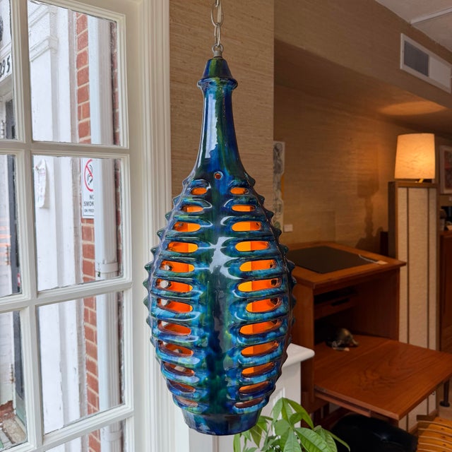 Tall, sculptural ceramic pendant with a deeply saturated blue and green lava-style glaze and pierced oval cutouts...