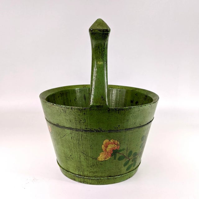 A green wooden hand painted bucket with a handle. This might’ve been used to hold water and wash vegetables.
