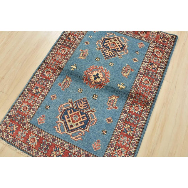 A tribal Caucasian Kazak rug is hand-knotted with an all-wool pile on a cotton foundation. This oriental rug features a...