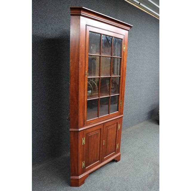 Henkel Harris corner cabinet in wild black cherry with glass-paneled upper doors and paneled lower storage. Features a...
