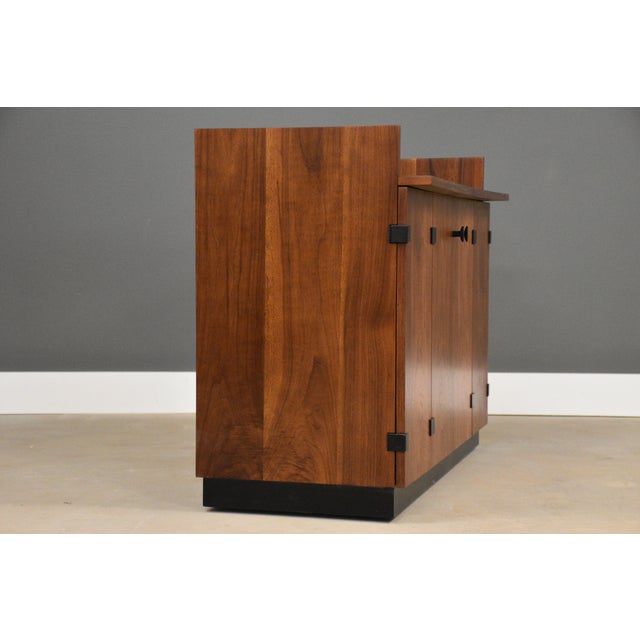 A mid century modern walnut rolling bar with black accents and a black formica top designed by Milo Baughman for...