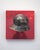 This artwork features a striking depiction of a metallic helmet set against a bold red background. The glossy surface of...