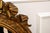 A large oval gilt wood wall mirror with an ornately carved frame topped with a decorative bow-and-ribbon crest and...