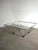 Striking square coffee table featuring a sculptural geometric chrome frame and clear glass top. The open metal...