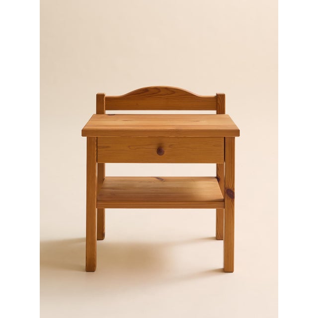 A charming pair of vintage pine bedside tables featuring a simple, utilitarian silhouette softened by a gently curved...
