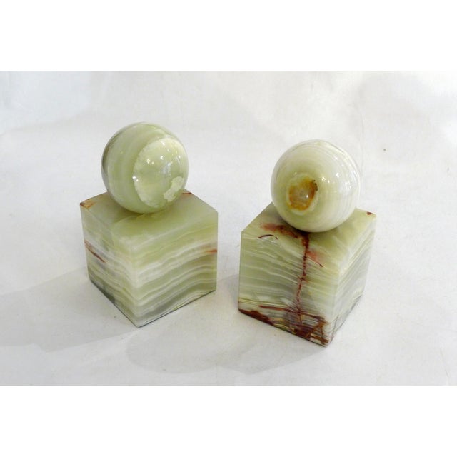 Pair of sculptural modernist bookends: cubic base supporting a sphere Made entirely of marbled/veined ochre green onyx...