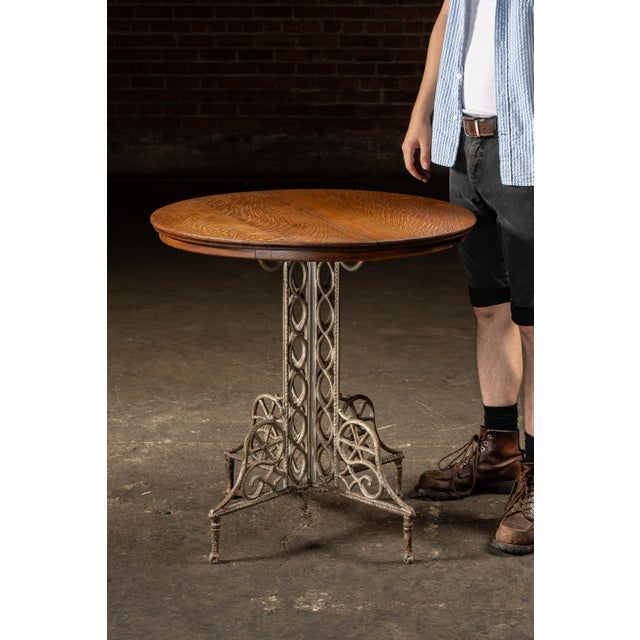 Round café-style table combining a cast metal base with a quarter-sawn oak top. The pedestal is formed from twin uprights...