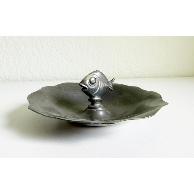 A pewter ashtray catchall dish that blends rustic and Art Deco modernism. Featuring a stylized fish rising from the center...