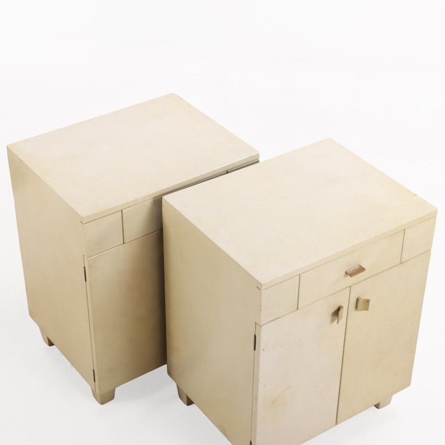 A stylish pair of mid-century cabinets or nightstands, circa 1960, clad in warm, natural parchment (pergamino). Each case...