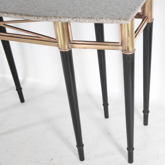 Stunning eight-legged console tables featuring a granite top, a brass band, and blackened wood legs. with their classical...