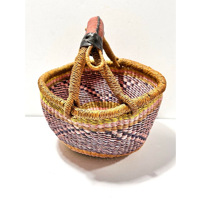 An authentic handwoven African Bolga basket crafted in Ghana, featuring rich earth-toned striping and a durable leather-...