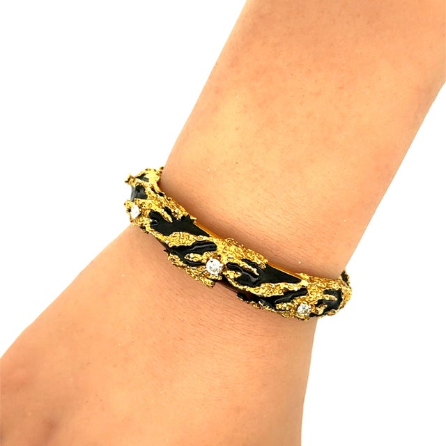 A contemporary cuff bracelet, featuring a textured design with intricate enamel detailing. The bracelet is adorned with...