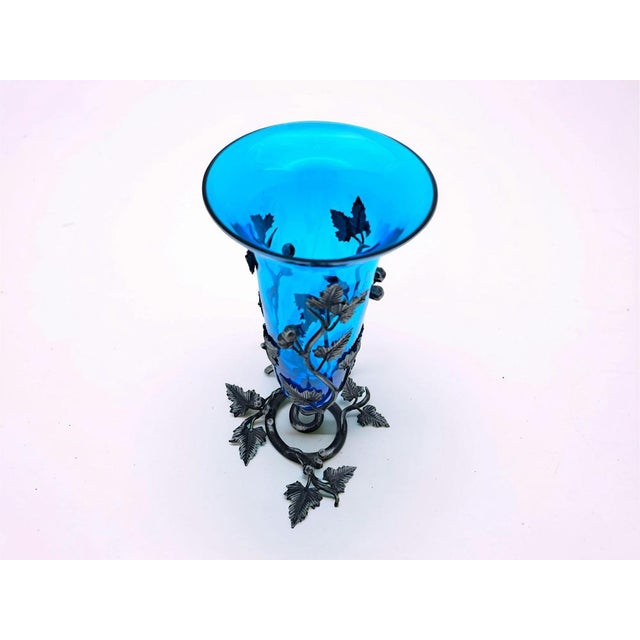 This blue Murano glass vase features a wrought iron base and decorations, enveloping the vase with grapevine and leaf...