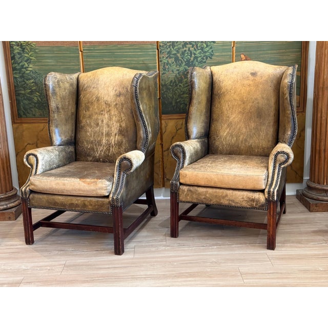A fine pair of 19th C. English wing back chairs upholstered in mottled brown leather with brass tack trim along the wings,...