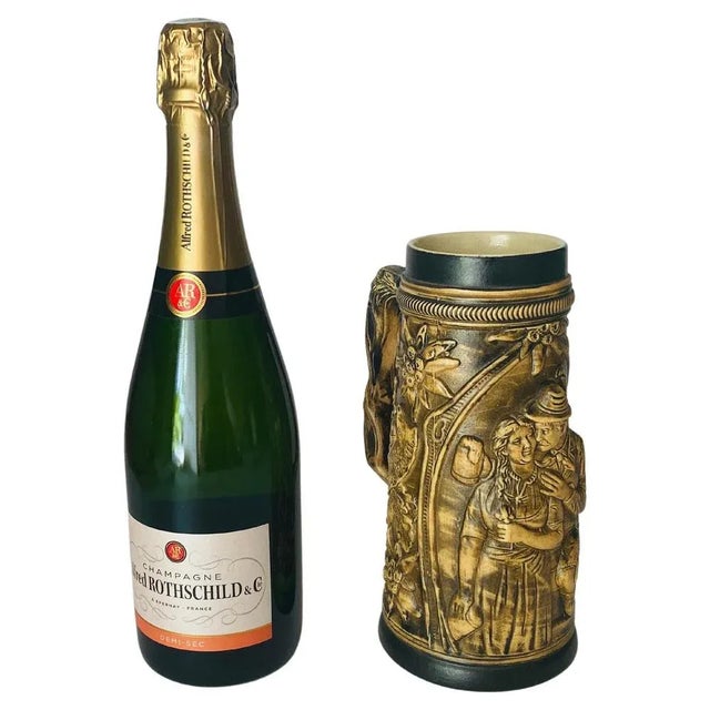 Cream colored ceramic stein with a curved ceramic handle with embossed floral designs. The body has one panel with a bas-...