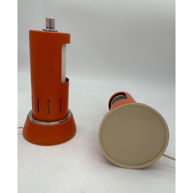 A pair of table lamps with a 1970s space-age design, featuring a cylindrical structure in orange lacquered metal with...