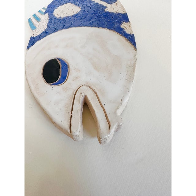 Charming handmade ceramic fish plaque featuring a richly textured blue-and-white glaze and whimsical folk art styling....
