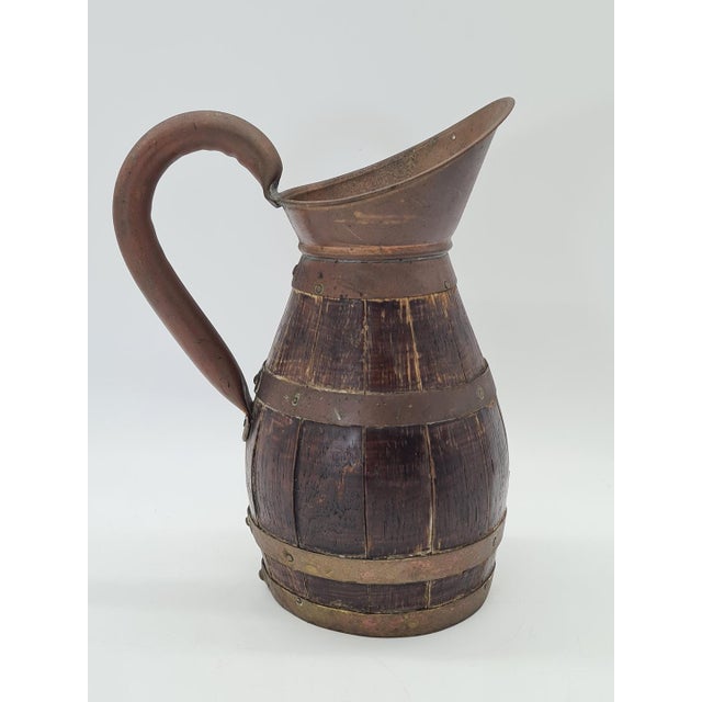 A unique, handcrafted wooden jug shaped like a small barrel, made using traditional cooperage techniques. The piece has a...