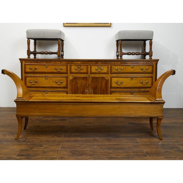 A French Restauration period walnut bench from the early 19th century, with lift-top seat, unusual out-scrolling arms and...