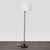 This Arhaus floor lamp features a sleek clear glass cylinder base with a sturdy black foundation and a simple white drum...