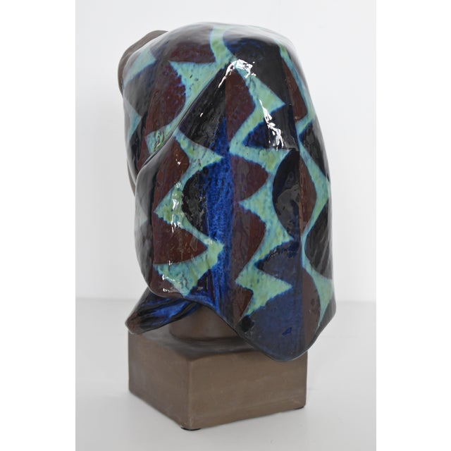 Terracotta bust in the shape of a womans head with a headscarf. Partially decorated with blue, purple and green glaze....