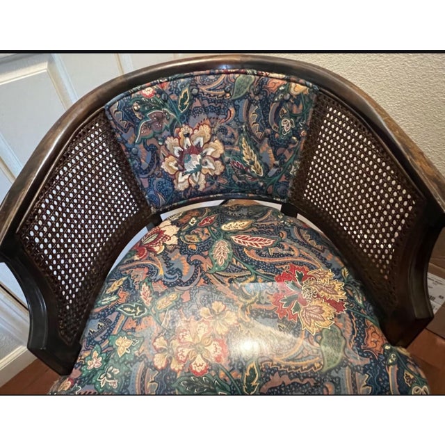 A striking vintage barrel-back accent chair featuring a gracefully curved dark wood frame, woven cane side panels, and...