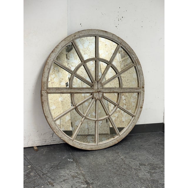 Design Plus Gallery presents a Segmented Radial Antiqued Mirror. The mirror has a circular wooden frame with a timeworn...