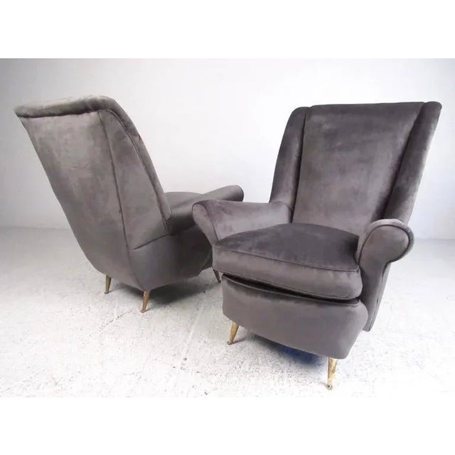 This vintage pair of Arredamenti ISA armchairs feature dramatic sculptural frames, tapered brass legs, and plush suede-...