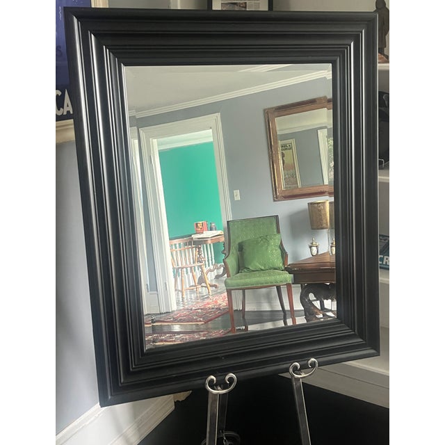 A sculptural black-framed wall mirror from the 1970s, featuring crisp bevel-edge glass and mid-century architectural form...