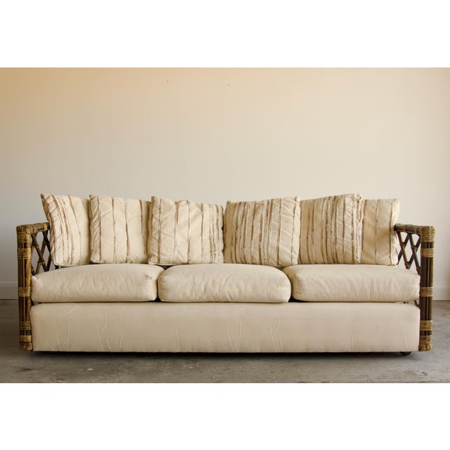 A striking vintage sofa framed in rich, dark-stained rattan, with open trellis lattice side panels that give it an airy,...
