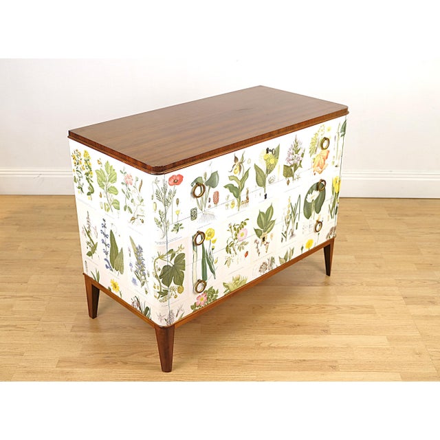 A refined statement dresser lavishly dressed in botanical plates from Nordens Flora by CAM Lindman, where each panel...