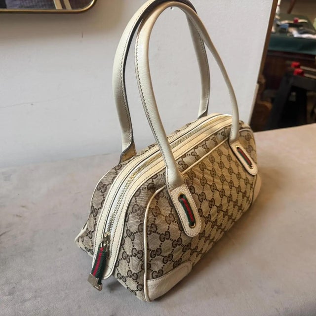 This vintage Gucci Princy shoulder bag crafted in classic beige and ebony GG monogram canvas features ivory cream leather...