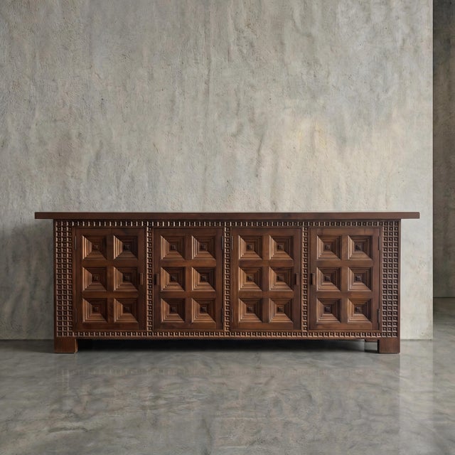 Deeply carved geometric motifs define the monumental facade of this 1960s Spanish sideboard, creating a rhythmic play of...