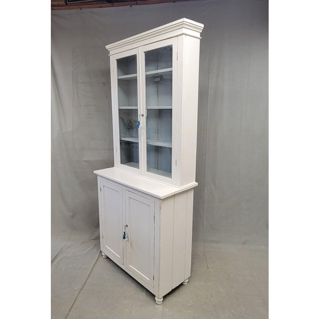 A beautiful, classic antique 1920s handmade English country painted two piece cabinet with old glass doors on the top and...