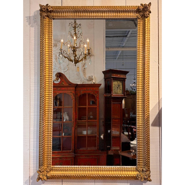 Louis XVI giltwood mirror with ribbed and rope twist moldings and carved floral clusters at each corner, framing an old...