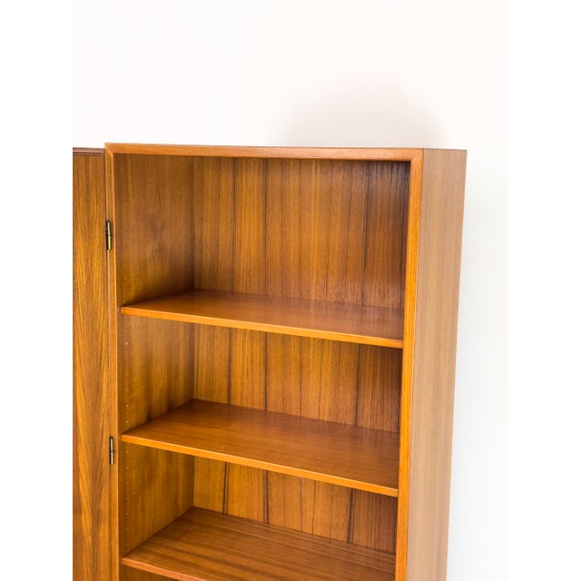 Exceptional narrow sideboard. Teak-veneered body with solid teak doors and veneered panels. Upper cabinet with three...