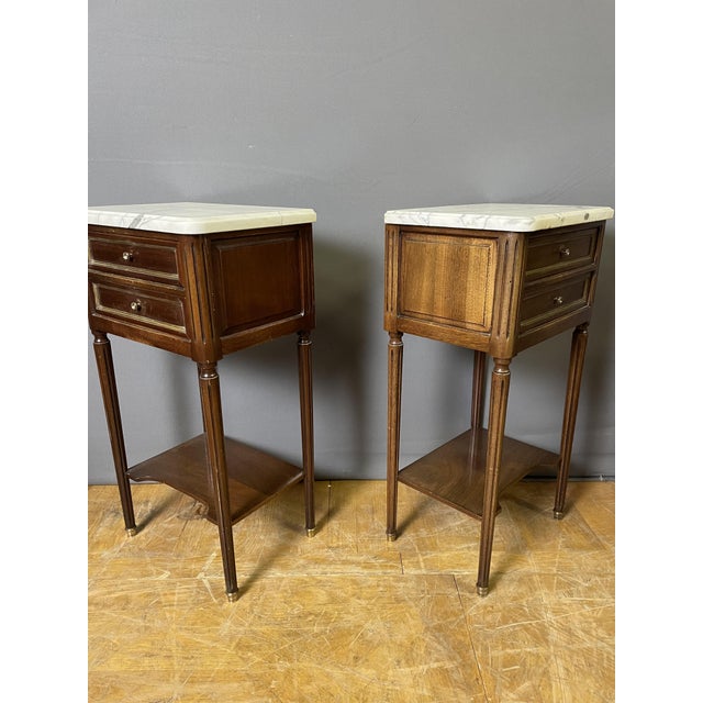 A pair of Louis XVI style bedside tables in mahogany-stained wood, each with two drawers in the front, fluted legs ending...