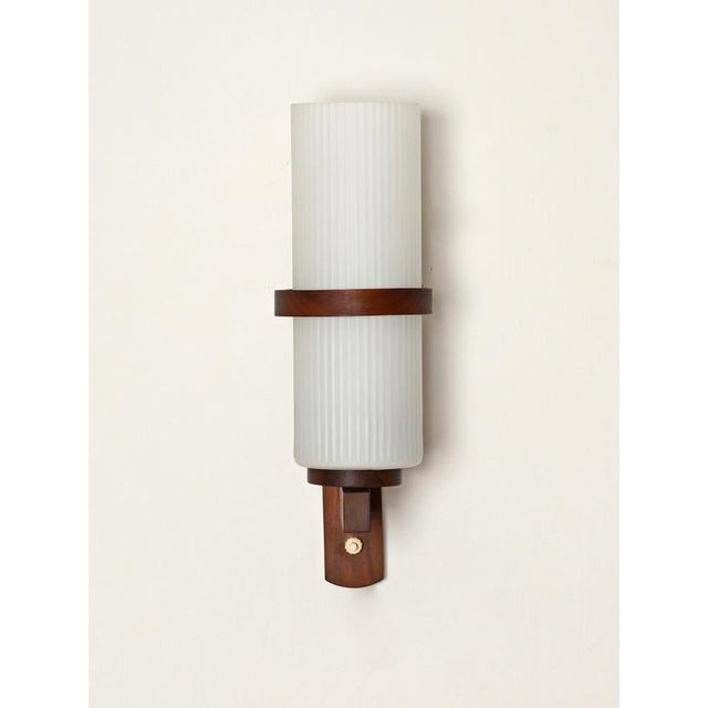 Elegant and unique mid-century wall sconce crafted from solid teak wood and completed by a gorgeous ribbed opaline glass...