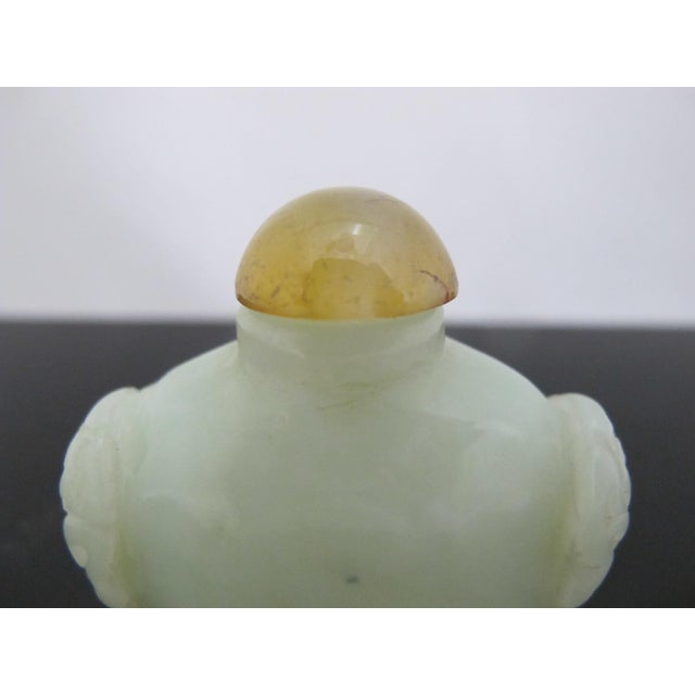 Antique Chinese hand-carved jade snuff bottle featuring a pale celadon hue and symmetrical carved mock mask ring handles....