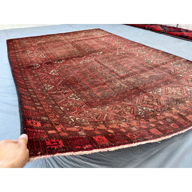 This hand-knotted Adraskan Baluch rug features a rich burgundy field divided into two paneled compartments, each framed by...