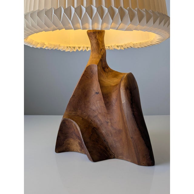 A sculptural table lamp carved from a single piece of solid olive wood. Its asymmetrical, free-form structure is defined...