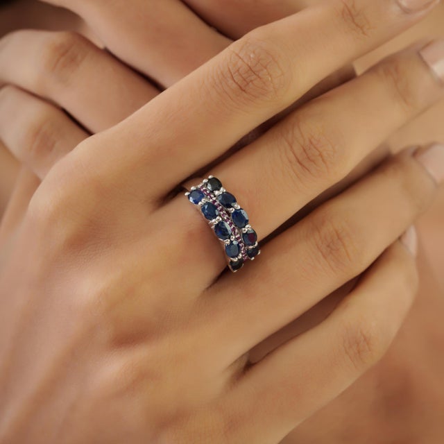 This elegant multi-row band ring features 2.29 carats of oval blue sapphires accented with vibrant rubies, handcrafted in...