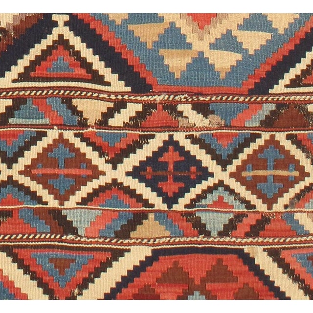 Vintage handwoven Caucasian Shirvan kilim featuring a bold geometric pattern. The vibrant color palette includes shades of...