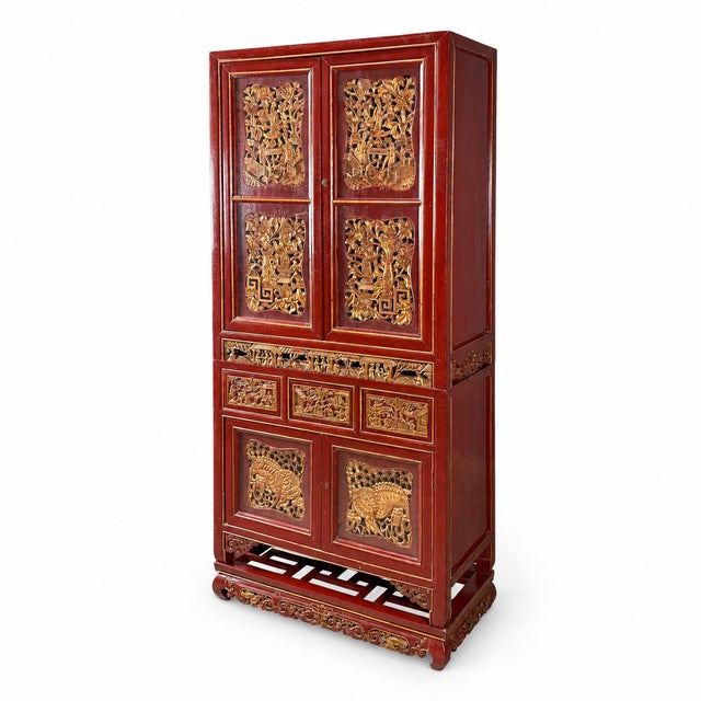 Red lacquered cabinet with gilt carved panels depicting animals and foliage, set on a low openwork stand. Upper cabinet,...