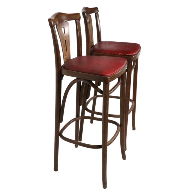 Pair of early - mid 20th century bentwood bar stools, by Thonet. The stools feature a pierce work slat back mounted in a...